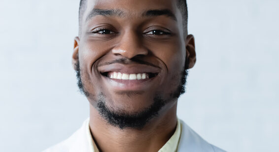 Nahaufnahme eines lächelnden jungen Mannes in einem weißen Hemd vor einem hellblauen Hintergrund.