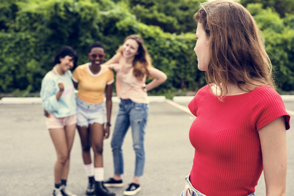 Vier junge Frauen unterhalten sich im Freien, wobei eine von der Kamera abgewandt ist und die anderen ihr zulächeln.